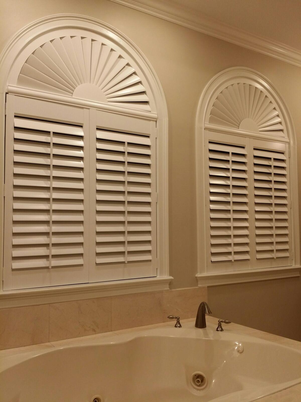 Arched white plantation shutters above a bathtub