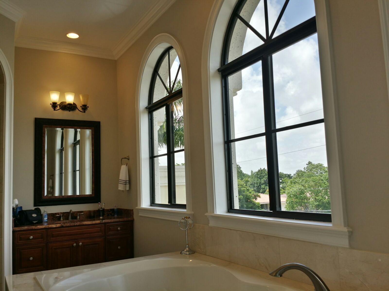Uncovered arched windows beside a bathtub and vanity