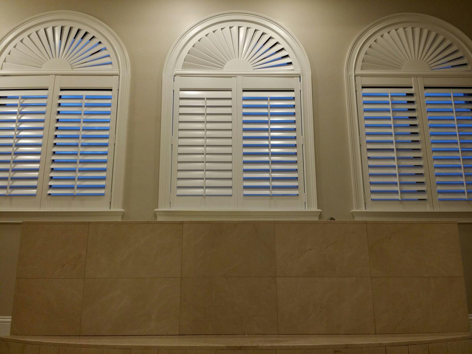White plantation shutters with fan-shaped tops on three arched bathroom windows